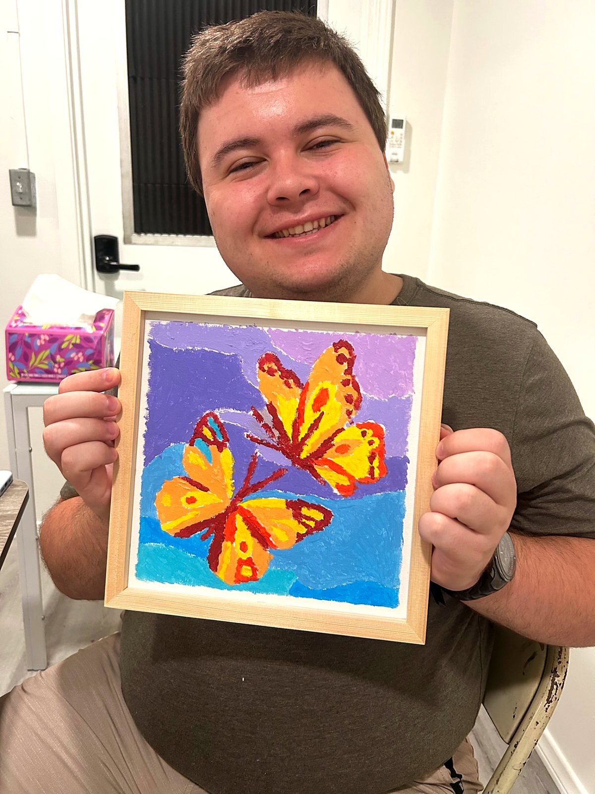 A participant holding up a framed butterfly painting they finished