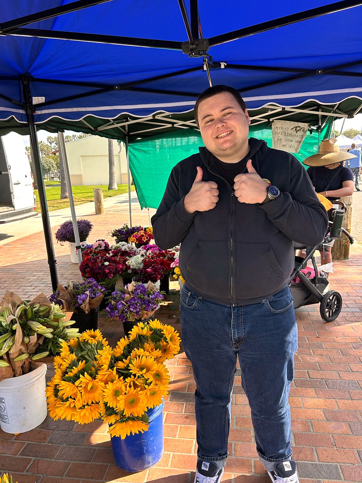 A participant standing with buckets of sunflowers at an outdoor market